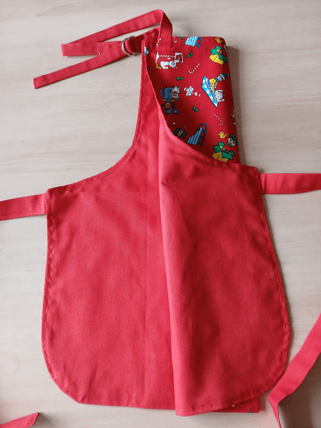 Childs Kitchen Play Apron Festive Patterned Cotton Fabric with Front pocket and Red lining, waist ties and adjustable neck ties