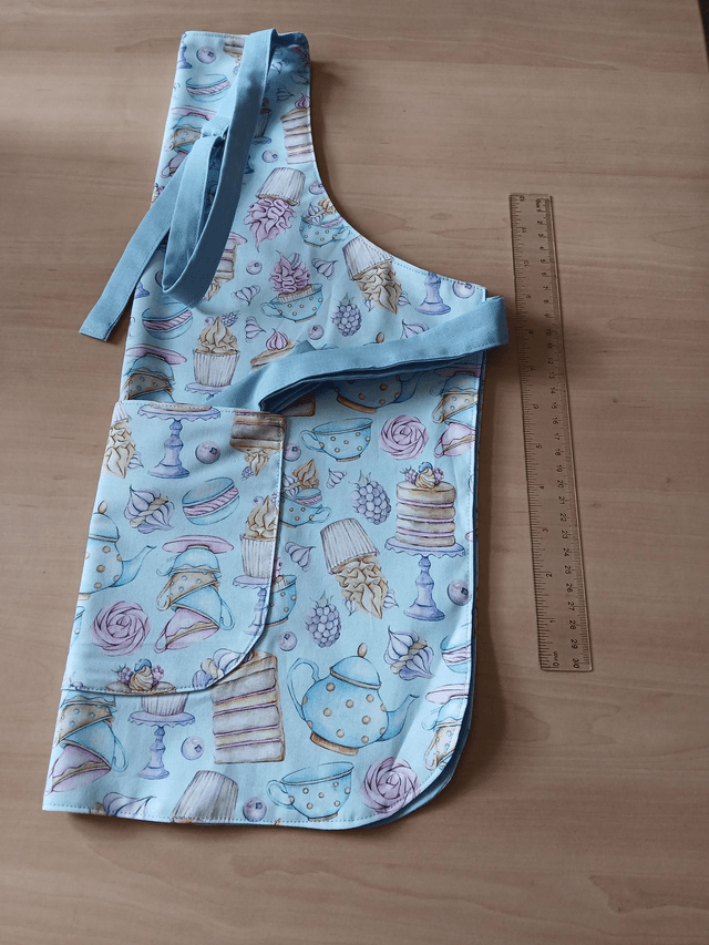 Childs Kitchen/Play Apron Three Wishes Frosted Fancies Cotton Fabric with lined Front pocket and pale blue lining.