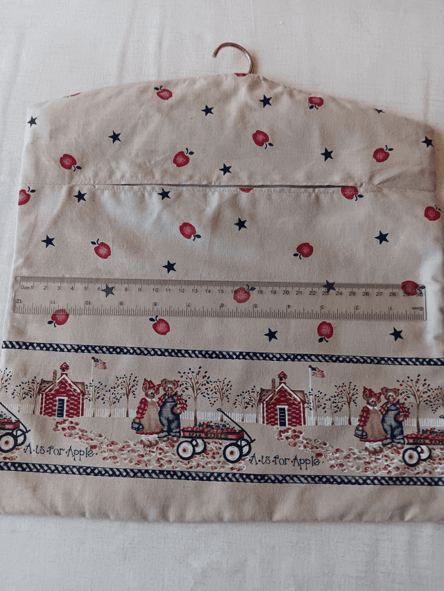 Hand made Peg Bag with wooden coat hanger. Apples print fabric with a picture border and plain beige lining.